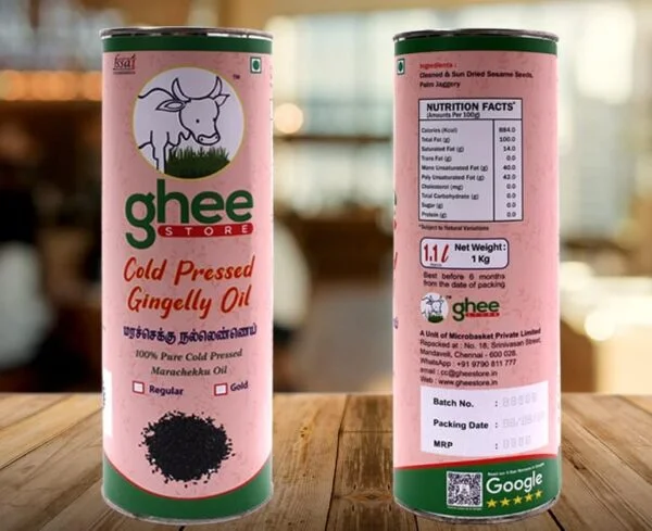 A cylindrical container of cold-pressed gingelly oil, featuring a cow logo and product information in English and another language. The label indicates it is 100% pure, with nutritional facts on one side and details including net weight, batch number, and packing date on the other. The container is placed on a wooden surface.